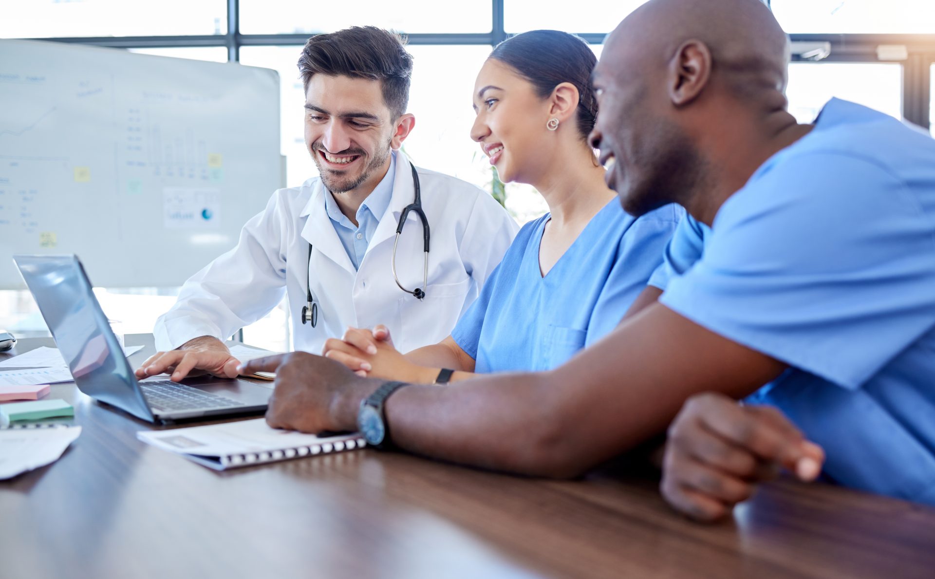 Ein Arzt und zwei Medizinische Fachangestellte sitzen lachend an einem Notebook